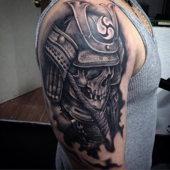 tânăr cu o mână care deține un tatuaj negru mare cu o armură japoneză și un craniu pentru tatuaj