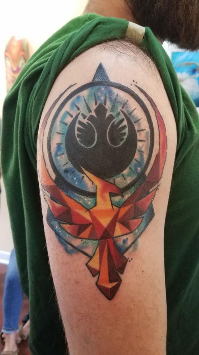 un bărbat cu bard brun - o mână cu un tatuaj mare cu un logo de războaie stea și o pasăre portocalie