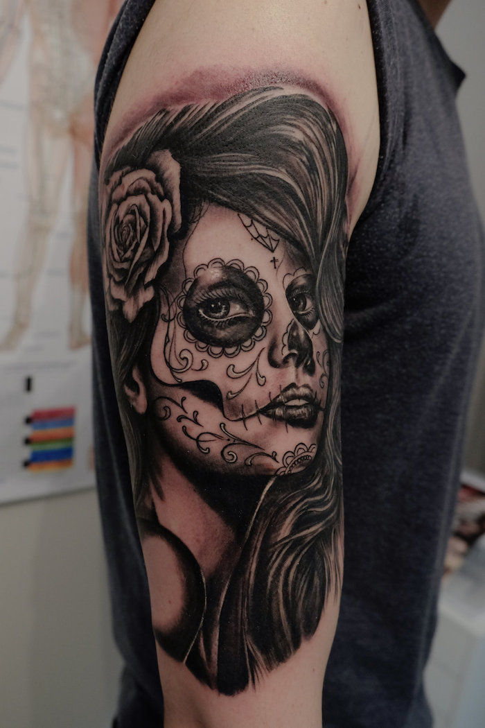 uomo con un tatuaggio la catrina con una rosa bianca e una giovane donna deceduta con le labbra nere