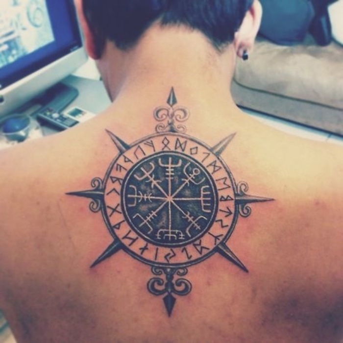 tukaj je moški z velikim, črnim, sodobnim tetovažem s črnim kompasom na hrbtu in uhani
