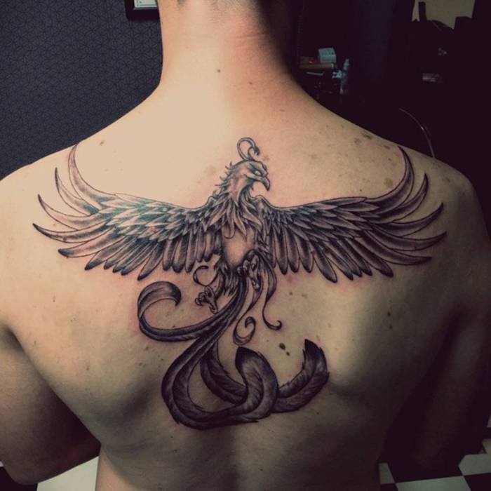Tatuaż feniksa z powrotem - człowiek z czarnym tatuażem z latającym czarnym feniksem z długimi czarnymi piórami