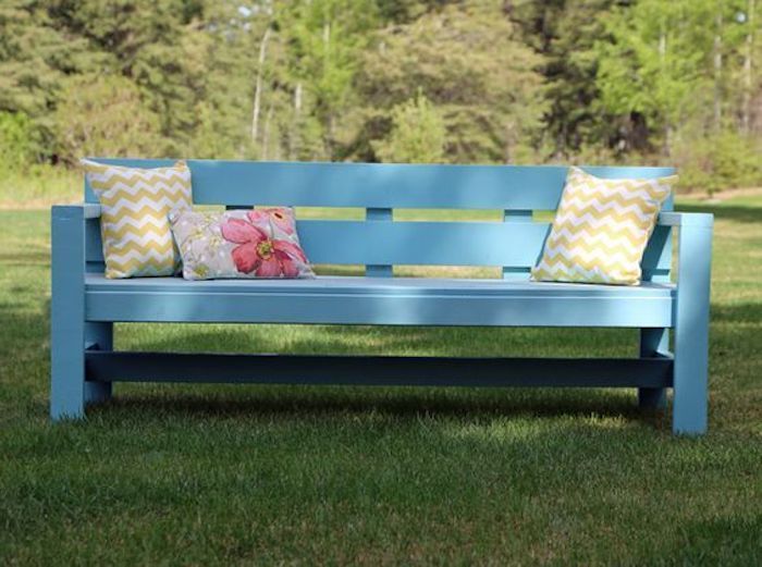 giardino con erba e alberi - una piccola panchina da giardino blu con due cuscini gialli e un piccolo cuscino con un fiore rosa