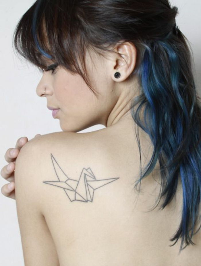 Ecco una giovane donna con i capelli blu e un piccolo tatuaggio con origami sulla scapola: una colomba bianca con origami volanti