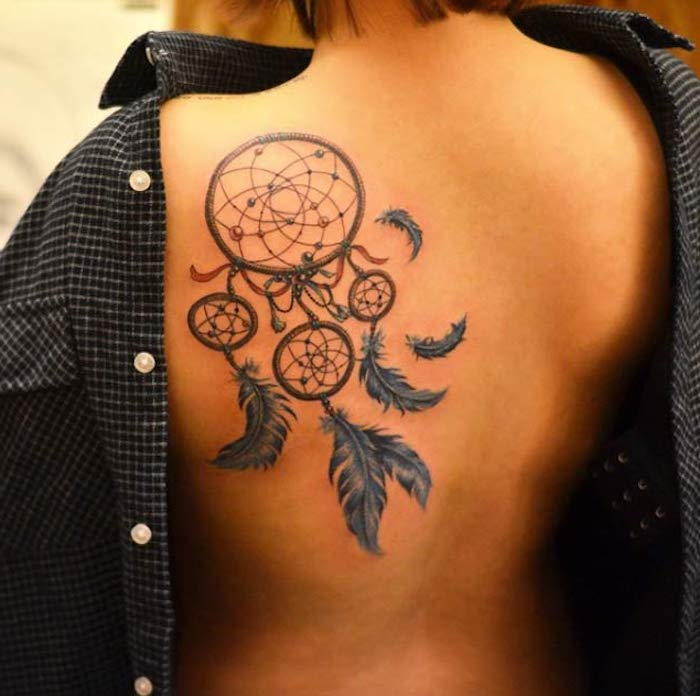 Dette er en tatovering på skulderbladet til en ung kvinne - tatovering med en stor svart drømfanger og blå fjer