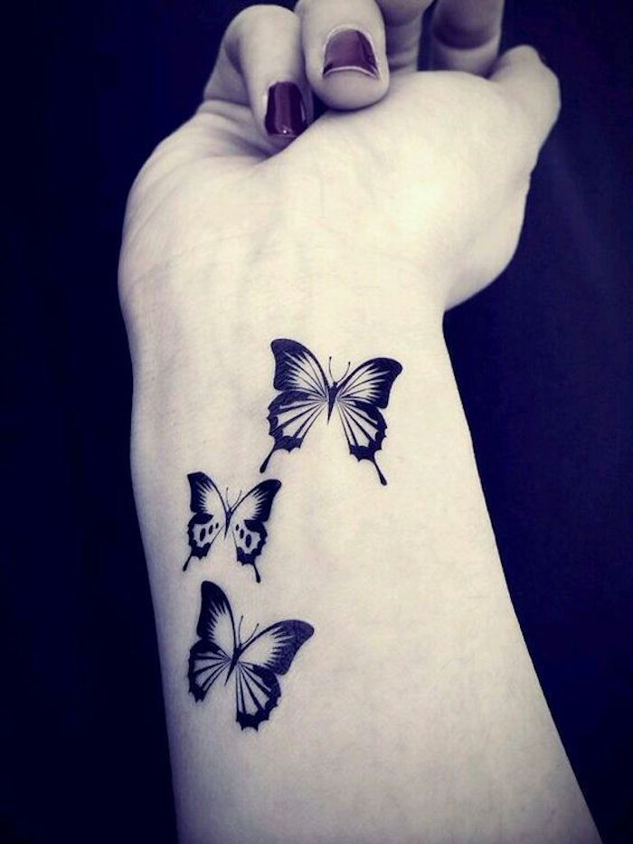 Dette er en av de beste ideene om temaet sommerfugltatovering som du virkelig kan glede deg over - tre små, svarte, flygende sommerfugler på håndleddet av en ung kvinnes hånd