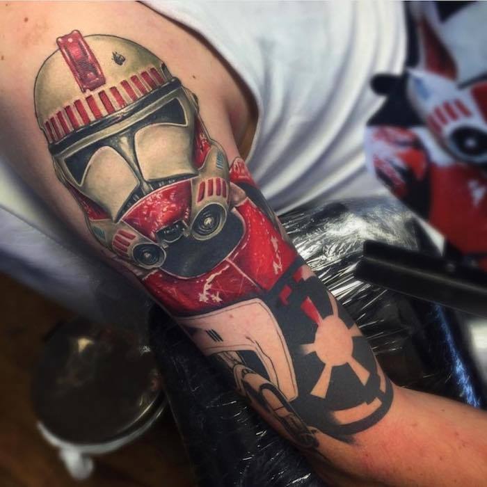 Un bărbat cu o mână care deține un tatuaj de război stele, cu un robot roșu și un mic tatuaj războinic al stelelor negre