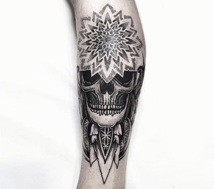 o mână cu un tatuaj de captură de vis, cu un craniu alb, cu ochi negri și dinți și pene albe