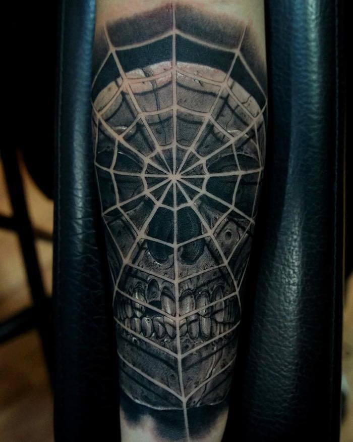 Hånd med en stor svart tatoveringskalle med en stor, hvit spindelvev