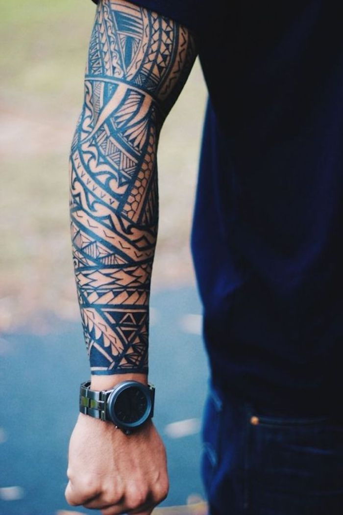 un uomo con pantaloni blu, orologio e un grande tatuaggio nero con molti motivi di tatuaggio maori neri