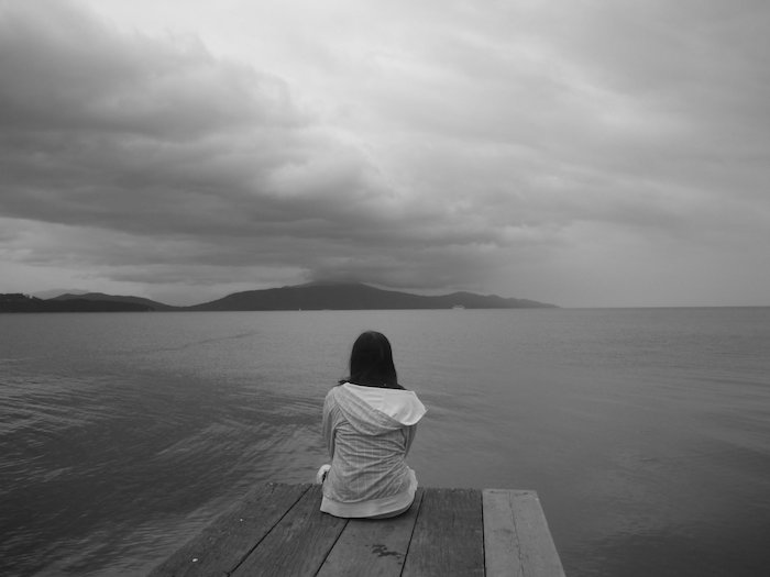 en sorglig ung kvinna och sjö och himmel med gråa moln - sorgliga bilder för att gråta