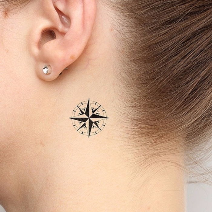 Tattoo kompas - Mlada ženska s tetovažo s črnim majhnim mini kompasom in uhanovima