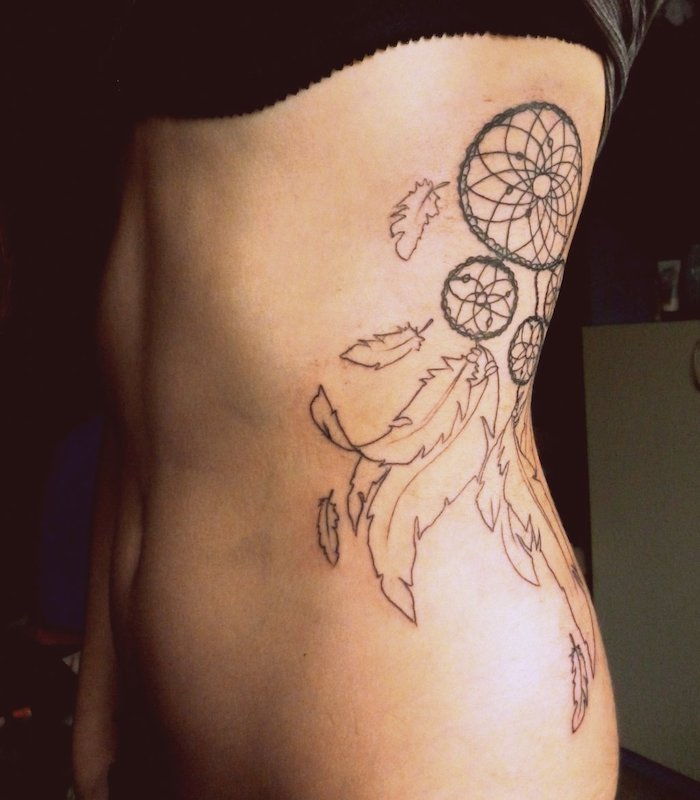 Aici veti gasi una dintre cele mai bune idei pentru un tatuaj cu un catcher de vis negru cu pene albe lungi - tatuaj pentru o femeie tânără