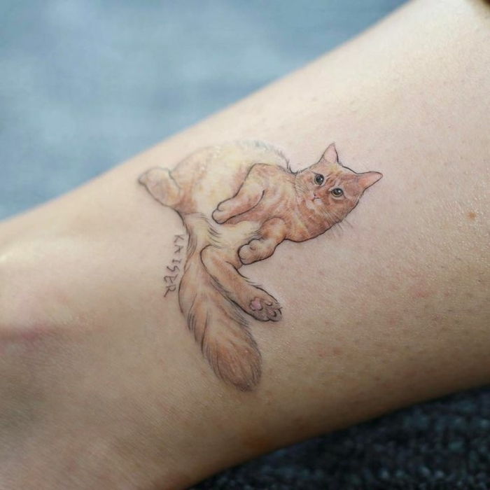 o mână cu o mare pisică de tatuaj - aici este o pisică portocalie cu ochi mari negri