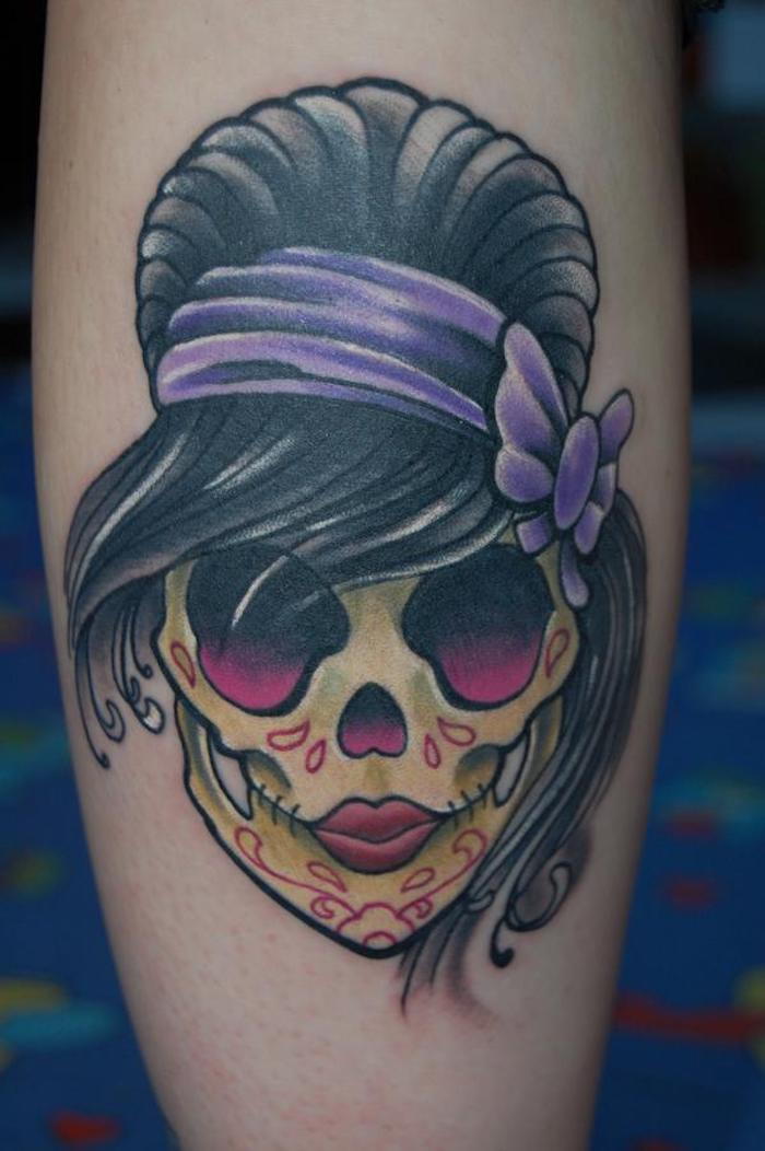 Ruka s tetovaním so žltou lebkou s fialovými očami a červenými pierami La Catrina obrázky