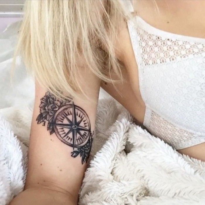 Aici veți găsi una dintre ideile noastre pentru un tatuaj negru mic, cu o busolă neagră și flori negre mici - o femeie tânără cu un tatuaj de busolă pe mâna ei