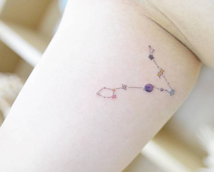 Hand met een tatoeage van een sterretje met een kleine paarse planeet en kleine blauwe en gele sterrensterren