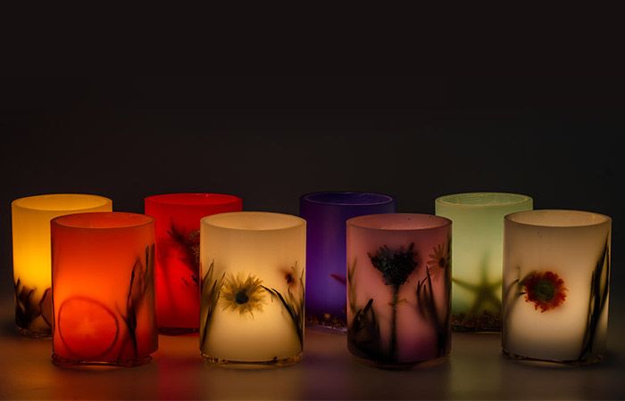 osiem świeczników wykonanych z matowego szkła barwionego z motywami roślinnymi, świeczników w różnych kolorach, palących się świec na czarnym tle