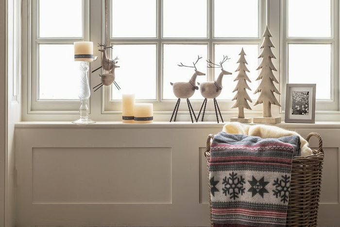 Fönster dekorera till jul - två julgranar av trä, målade i vitt, svart och vitt foto med grå ram, tre stora ljus, dekorerade med snöre, glas ljusstake, två rådjur siffror för Aufhöngen, två rådjur siffror av bomull och trä, stor korg med två filtar - en gul filt och en filt med snöflinga Mitove, vit vägg med träpanel
