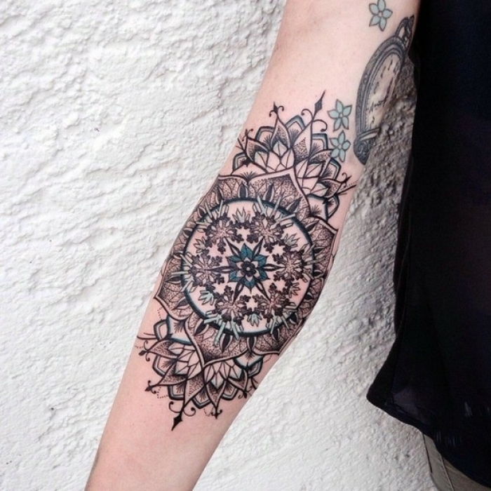 Kobieta z tatuażem pod pachami ze skomplikowanym wzorem w dwóch kolorach - czarnym i turkusowym niebieskim, niebieski kwiat w środku, małe turkusowe kwiaty na górnej stronie