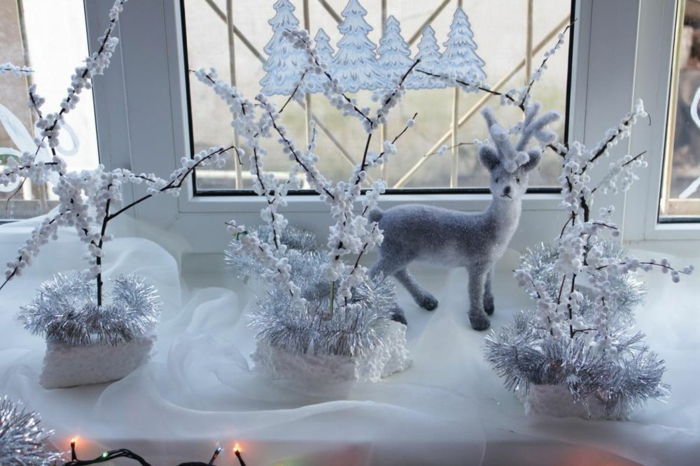Elegant Jul i vitt - tre trädgrenar, dekorerad med pop corn och silvergirlanger, lägg i tre Whites frigolitbitar, små vita hjortar siffra, som tillhandahålls av fönstret på en halvtransparent vit Tülldecke, julgran klistermärke på fönstret, julbelysning med små gula lampor