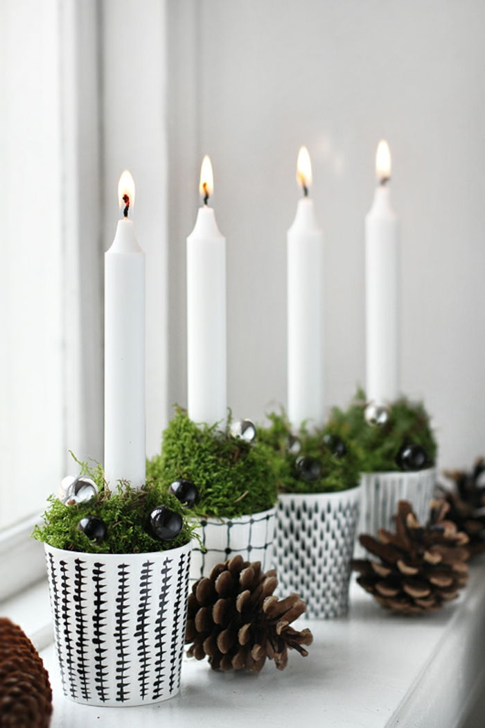 štyri osvetlené biele voskové sviečky v štyroch čiernych a bielych papierových pohároch naplnených čerstvou zelenou trávou a malými čiernymi guľami