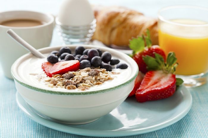 Muesliskål med yoghurt, jordbær og blåbær, kokt egg, appelsinjuice, croissant og kaffe til sunn frokost
