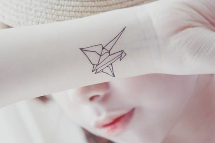 Ecco una giovane donna con un piccolo tatuaggio origami al polso - un piccolo uccello origami volante sulla mano