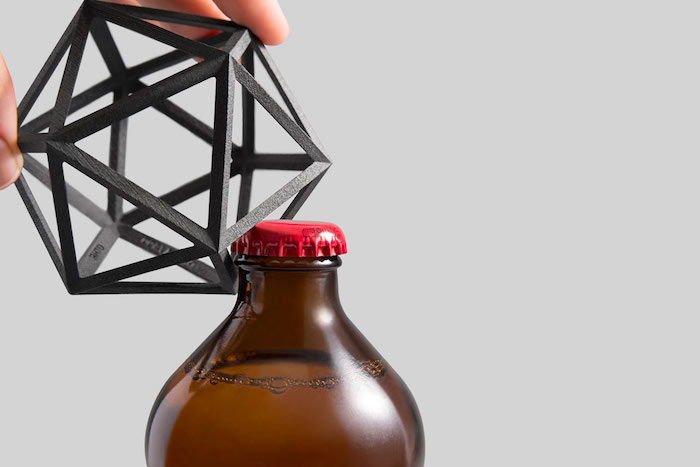 Designerski otwieracz do butelek wykonany ze stali nierdzewnej w kształcie wielokąta, butelka piwa z brązowego szkła z czerwoną metalową pokrywką, mężczyzna otwiera butelkę piwa
