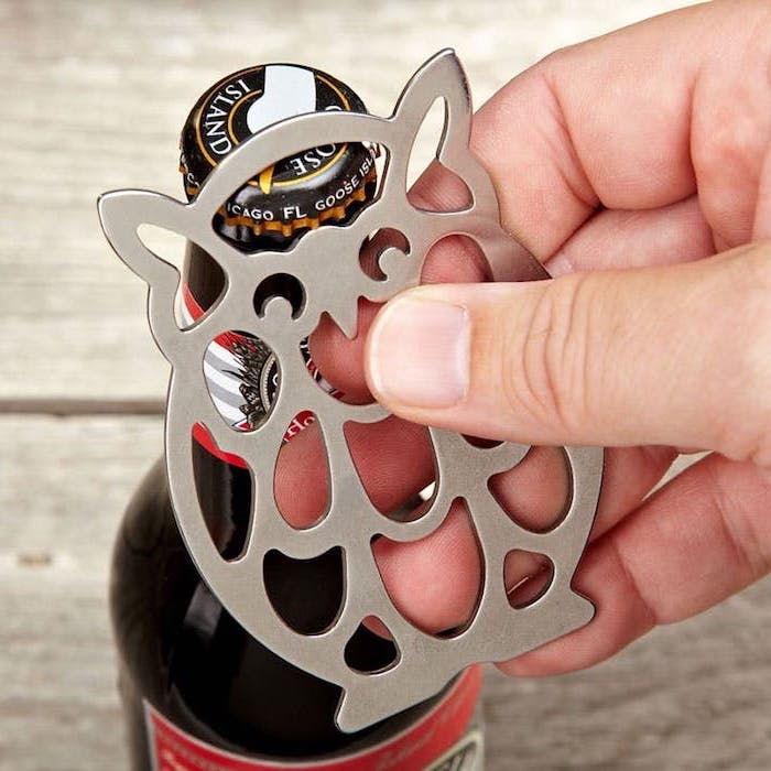 butelka ciemnego piwa z czerwoną etykietą, czarna metalowa pokrywa z białymi literami i złotym Kantem, otwieracz do piwa w kształcie sowy, mężczyzna z otwieraczem do piwa w prawej ręce