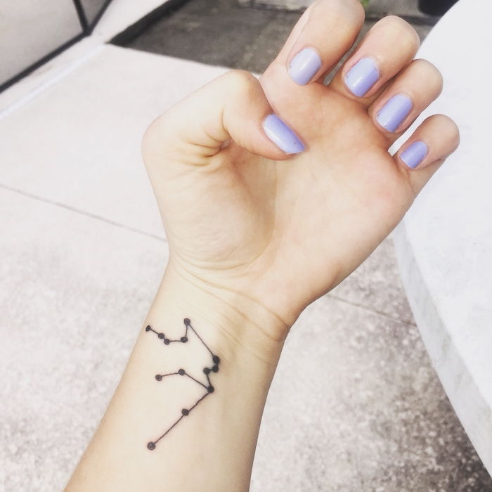 tetovanie hviezda pre ženy - ruku s purpurovým lakom na nechty a tetovanie s čiernym hviezdnym obrazom na zápästí