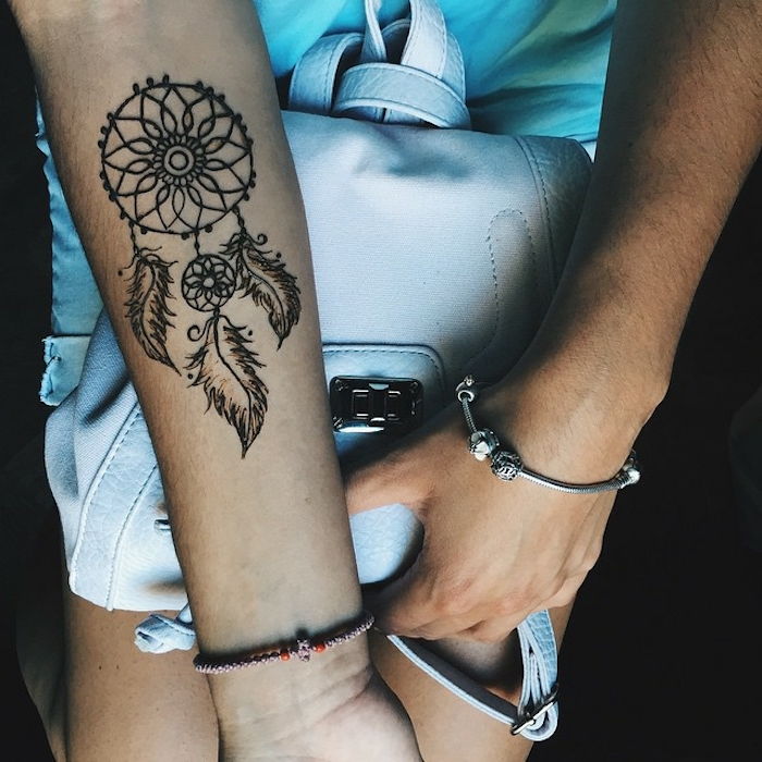 Qui troverai una mano con un tatuaggio da sogno con piume nere piccole e belle e una mano con un braccialetto