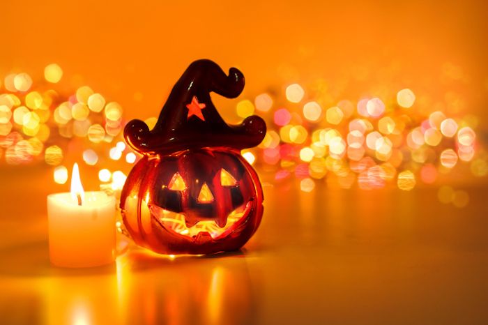 uma estatueta de vidro ao lado de uma vela e luzes brilhantes no fundo - fundo de Halloween