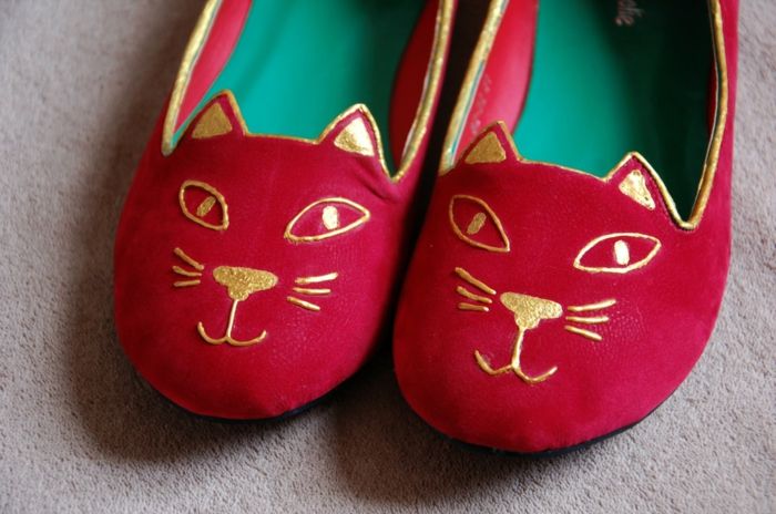 røde sko syr med et gyldent ornament som en kattens ansikt