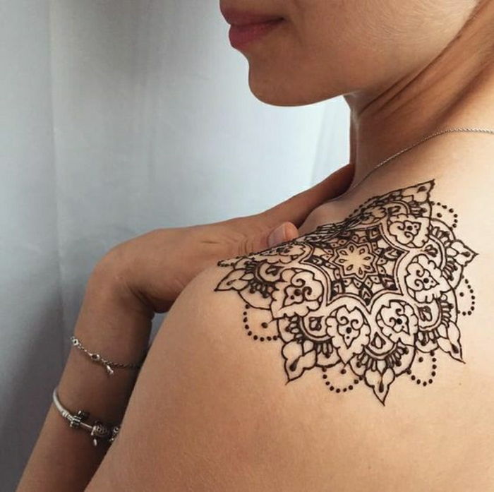 Kvinna med axeltatuering av henna, mandala tatuering i svart färg, silverarmband