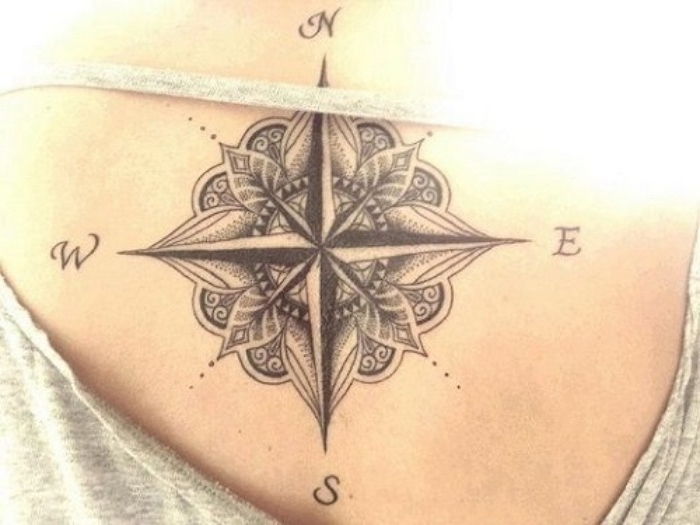 Czarny kompas z małymi czarnymi liśćmi - tatuaż na grzbiecie młodej kobiety