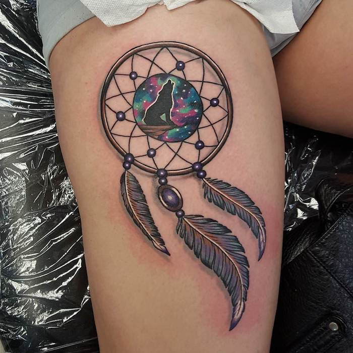 Tattoo med en vakker, svart, lille hylende ulv og en stor drømfanger og tre svarte fjær
