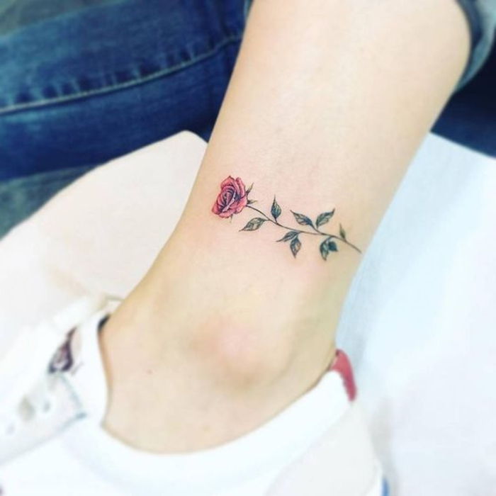 Ecco una gamba con una sneaker bianca e un piccolo tatuaggio con una rosa rossa con foglie verdi sulla caviglia