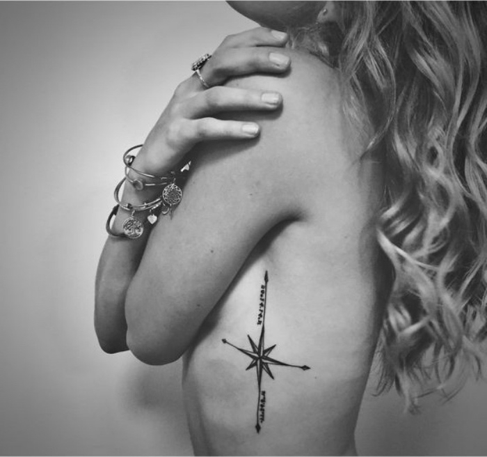 Kobieta z pierścieniami i małym eleganckim tatuażem kompasu z czarnymi strzałami