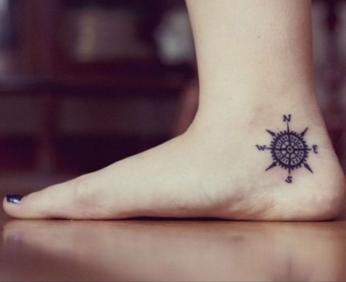 picior cu un lac de unghii albastru și un mic tatuaj negru mini cu o busolă neagră pe toc
