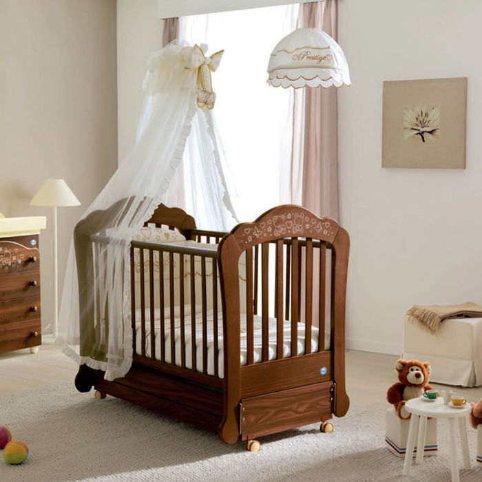 Pastelinių spalvų kūdikių kambarys, medinė lovelė su ratukais, baltas dangus, mažyliu stalu maitina arbatą