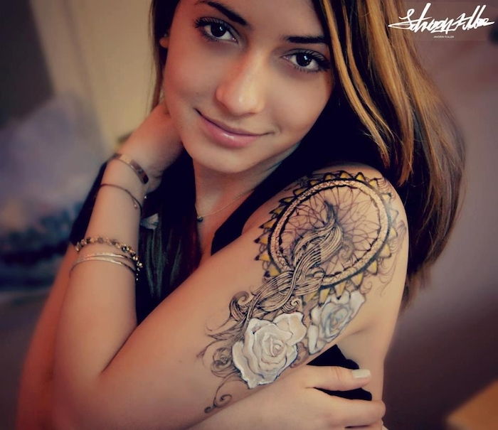 Her er en ung kvinne med en stor tatovering med en drømfanger med to hvite store roser på skulderen hennes