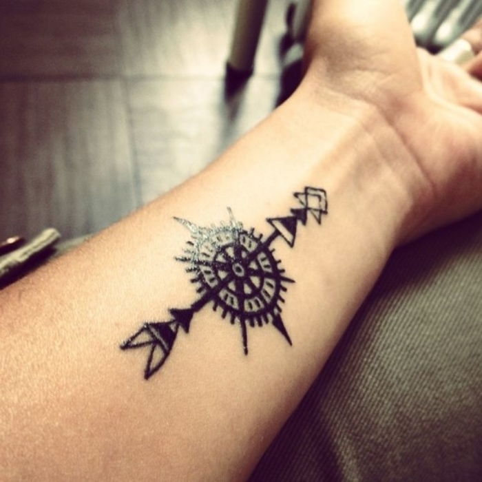 tatuaż kompasowy - ręka z czarnym tatuażem z czarną długą strzałą i małym czarnym kompasem - tatuaż na nadgarstku