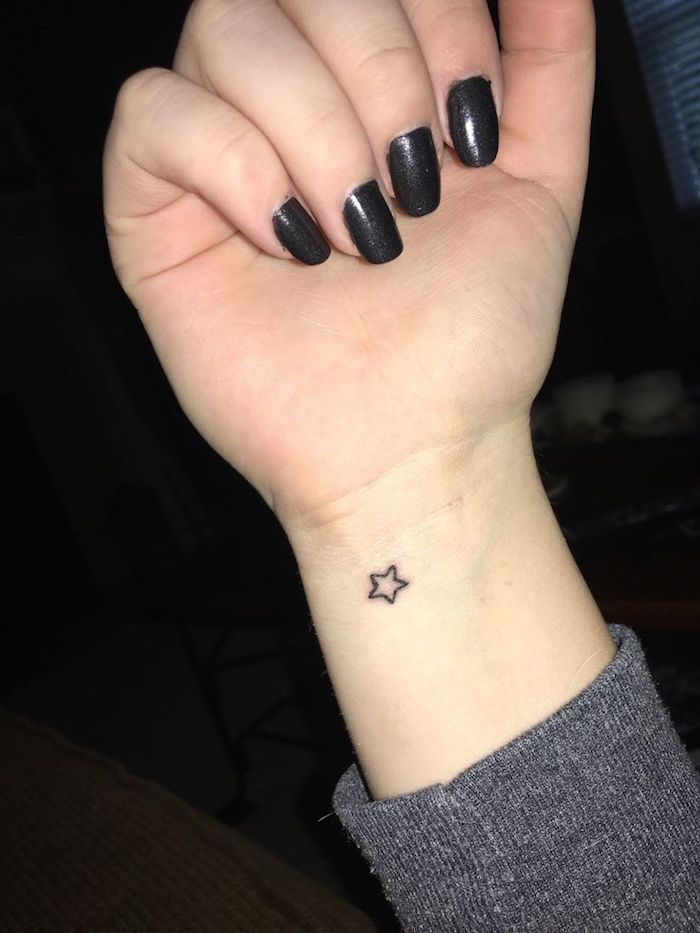 een hand met een kleine zwarte tatoeage met een kleine ster - hand met nagels met een zwarte nagellak
