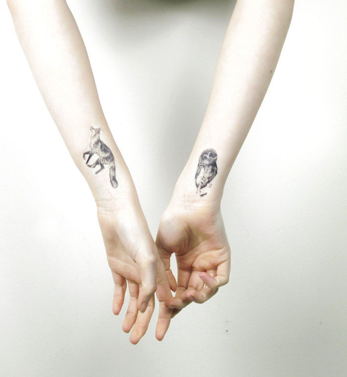 Hier zijn twee handen met kleine tatoeages op pols - uil en vos