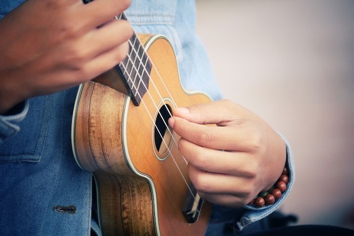 Mini gitara so štyrmi strunami z prírodných vlákien, deka s bielymi hranami, hudobný prehrávač s džínsovou košeľou a náramky vyrobené z drevených korálkov