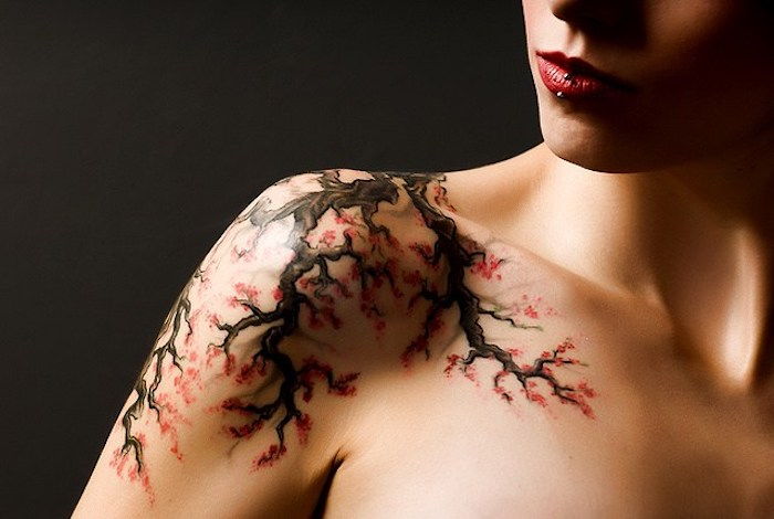 Femeie cu tatuaj de floare de cireș pe umăr, ramură cu flori roșii
