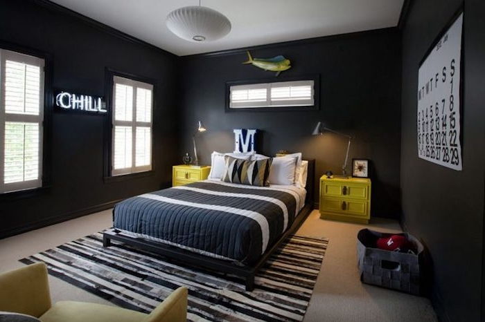 Jaunimo kambario dizainas, juodos dryžios sienos, geltonos naktinės stalelės, raidė M virš lovos