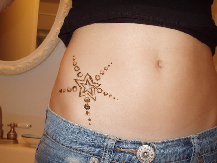 En ung kvinne med en svart tatovering med en liten svart stjerne og blå bukser - ide om temaet tatoveringsstjerne