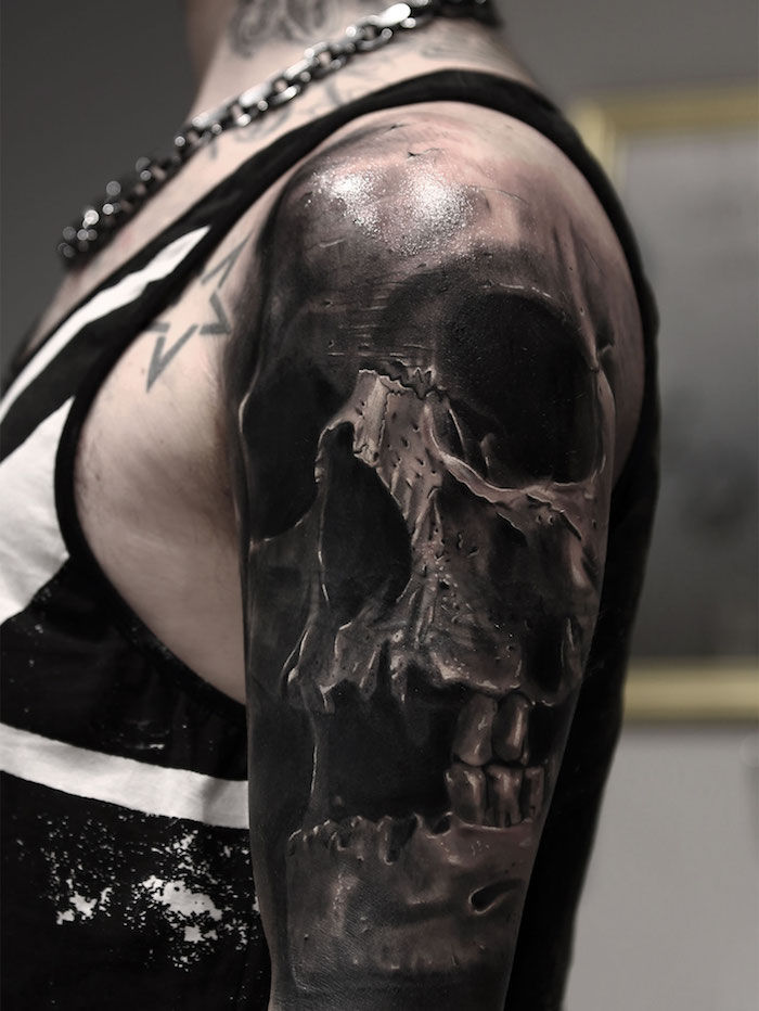 En hånd av en kvinne med en stjerne tattoo og en stor tatovering med en stor, svart hodeskalle med svarte øyne og tenner - kranietattovering