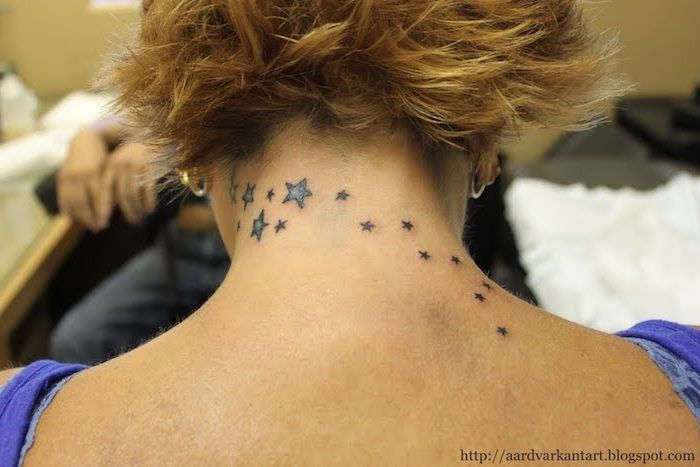 idee voor een sterrentattoo voor de vrouw - een zwarte tatoeage met kleine en grote zwarte en blauwe sterren op de rug